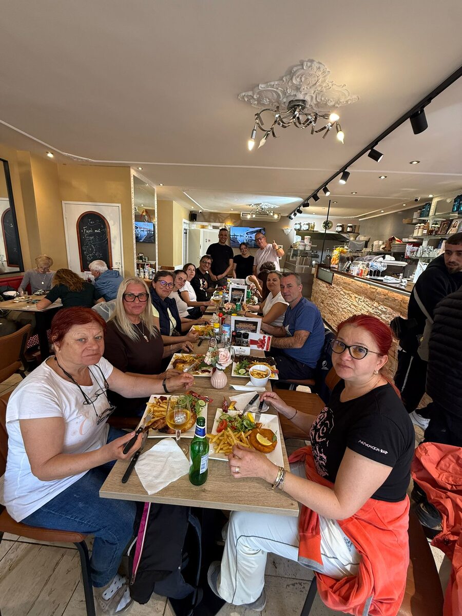 Een grote groep aan één lange tafel binnen bij Amarylles, met borden friet en salade voor zich en de toonbank erachter
