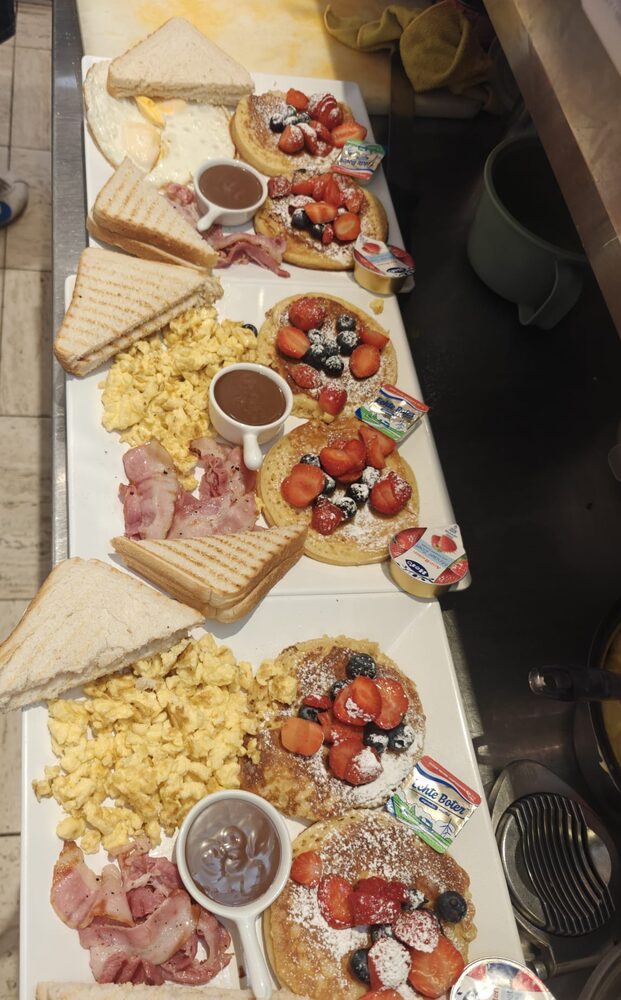 Twee Amerikaanse ontbijten met pannenkoeken, aardbeien, roerei, spek en toast