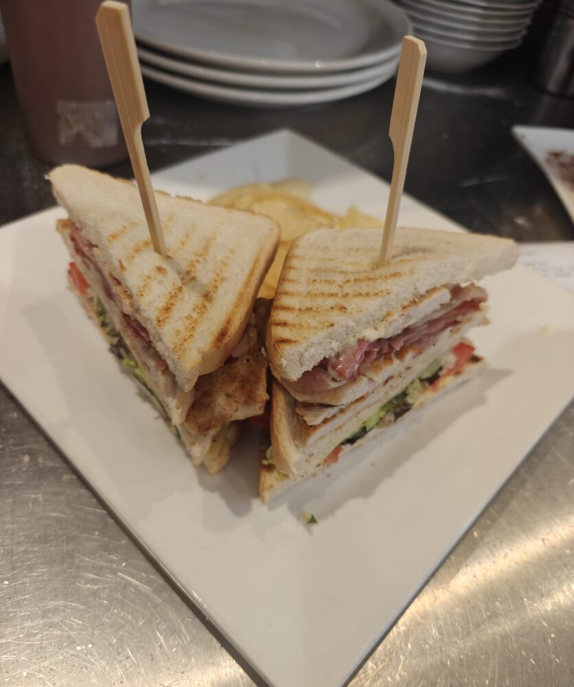 Een clubsandwich in vieren met prikkers, op een wit bord met chips