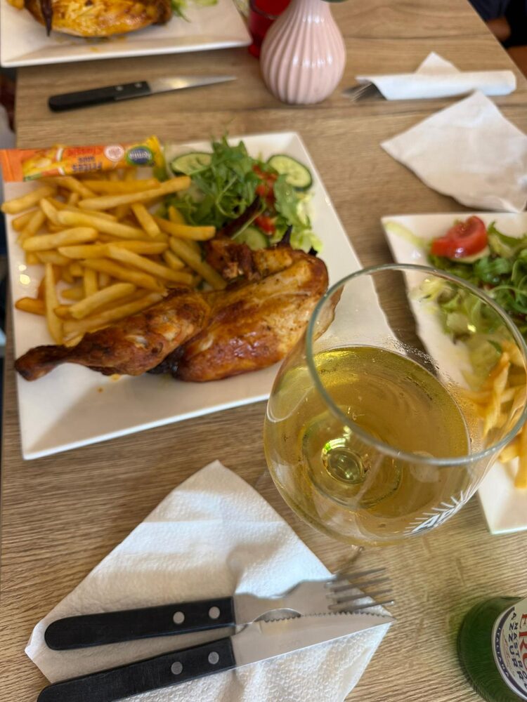 Een halve kip met friet en salade, met een glas witte wijn ernaast