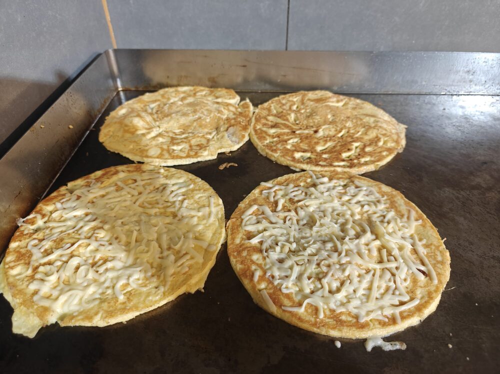 Vier Hollandse pannenkoeken op de bakplaat, twee met geraspte kaas