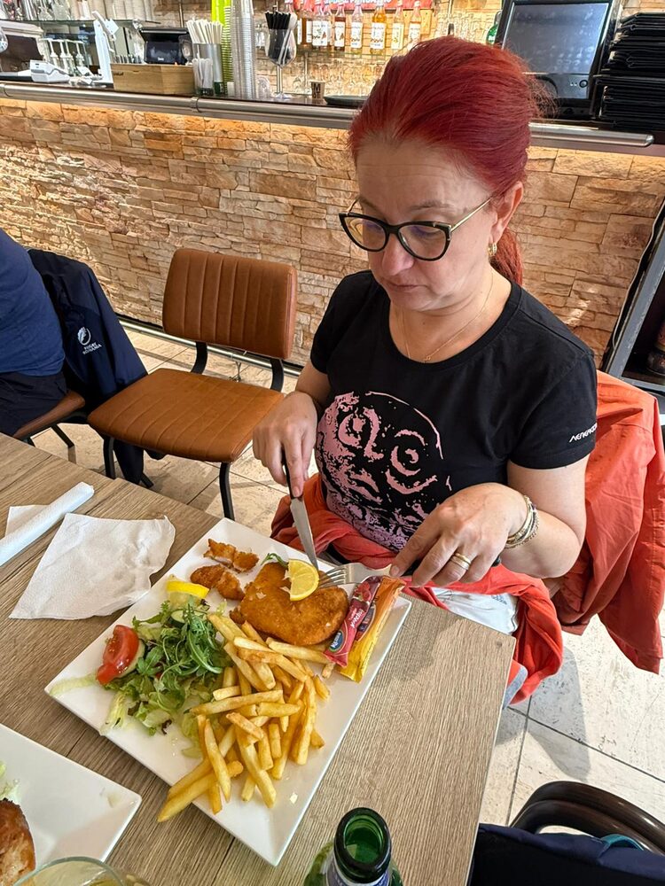 Een gast snijdt een kipschnitzel aan, met friet en salade, met de bar op de achtergrond