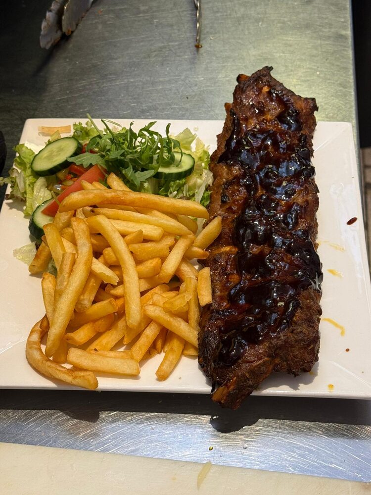 Een streng spareribs met glanzende saus, friet en gemengde salade op een wit bord